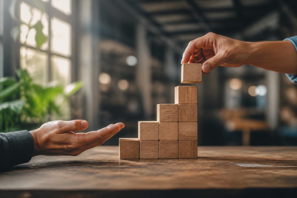 Des mains posent les marches d'un escalier de blocs en bois, symbole de la montée en compétence portée par chaque niveau de management